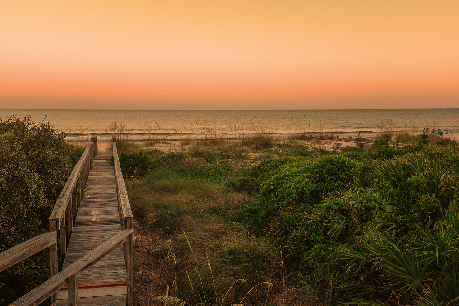 A boardwalk in the Gulf Coast leading down to the beach and ocean at sunset.